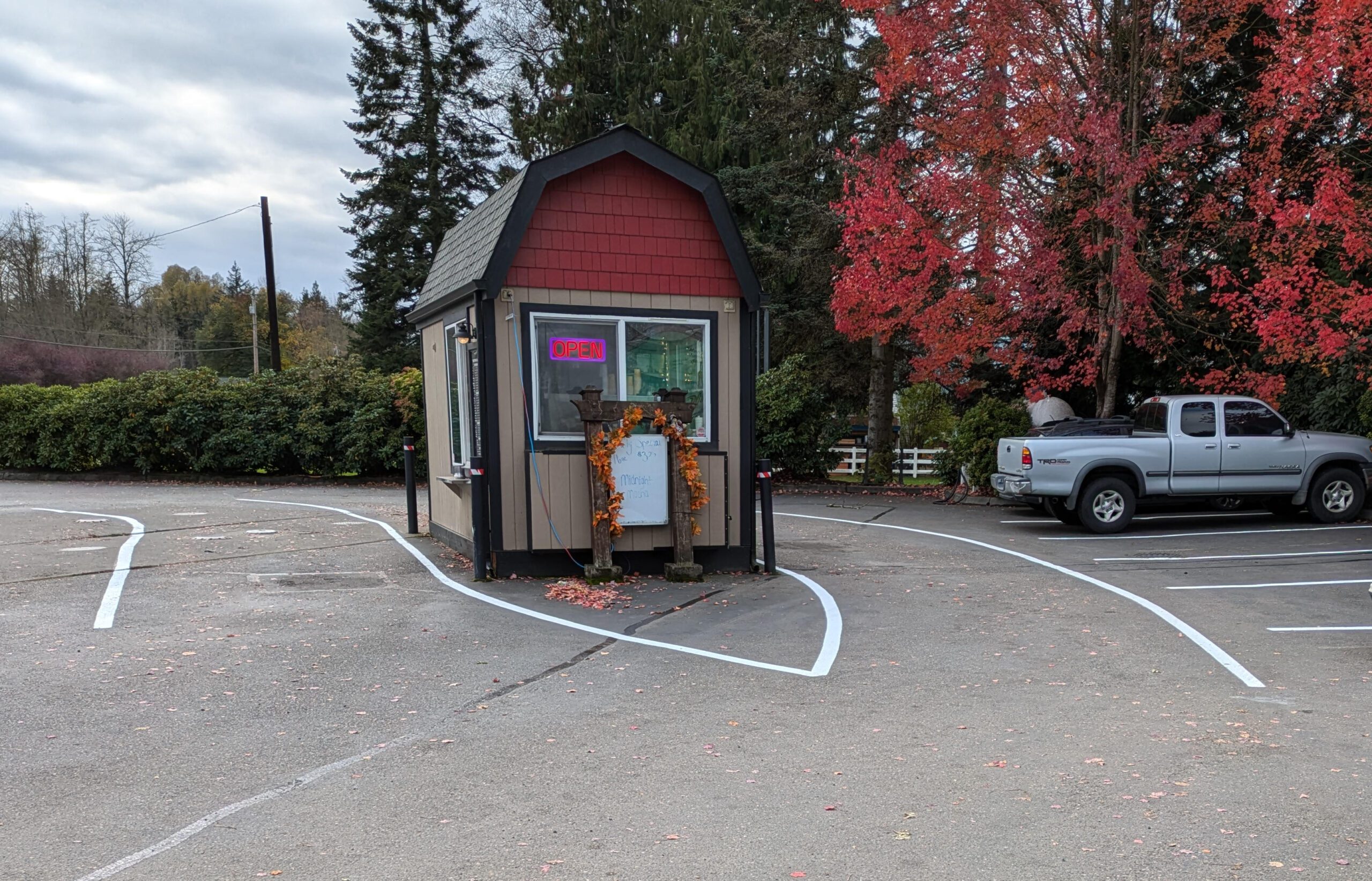 Freshly striped drive-thru lane and parking lot at a small coffee stand in Redmond, WA, completed by 1-800-STRIPER of Bellevue. The bright white lines improve traffic flow and organization for customers. Vibrant autumn trees in the background highlight the seasonal charm of Redmond.